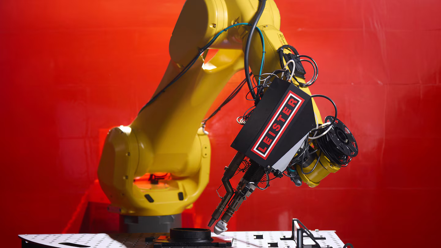 Braço robótico FANUC equipado com extrusora Leister WELDPLAST 200-i, realizando soldagem plástica de alta precisão