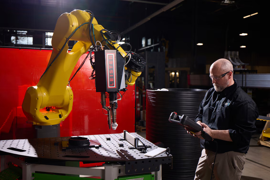 Engenheiro operando painel de controle enquanto acompanha robô FANUC com extrusora Leister WELDPLAST 200-i