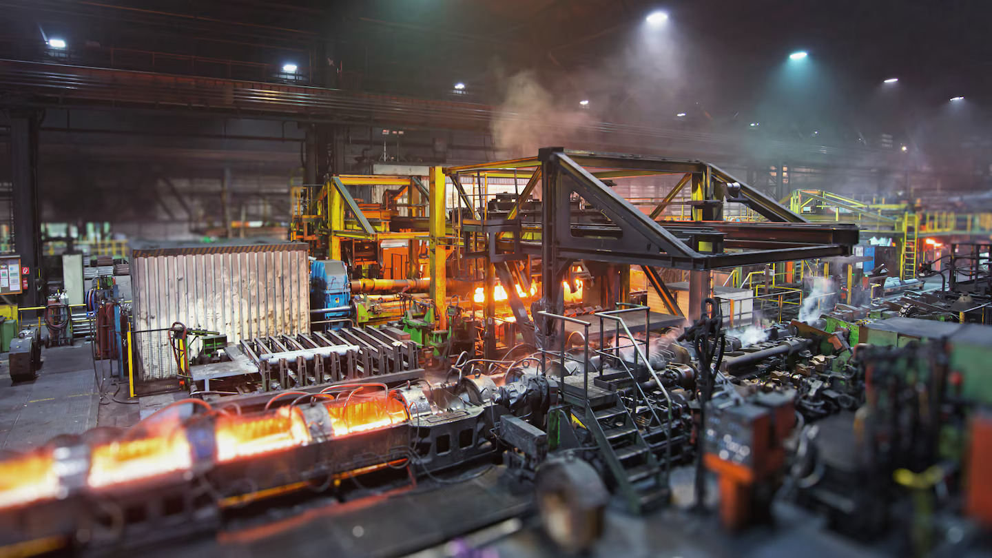 Usina siderúrgica com máquinas em operação, mostrando o ambiente desafiador onde os sistemas de secagem Leister ajudam a manter a confiabilidade elétrica