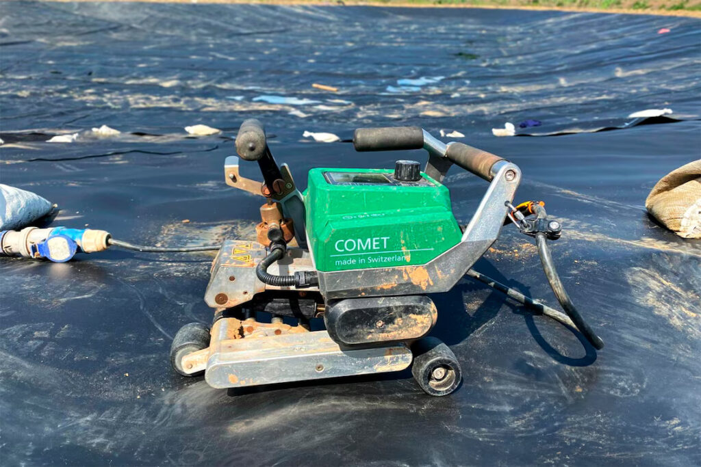 Soldadora automática Leister COMET 700 sobre geomembrana de PEAD durante a soldagem de longas emendas para impermeabilização de um lago em Darlington, Reino Unido