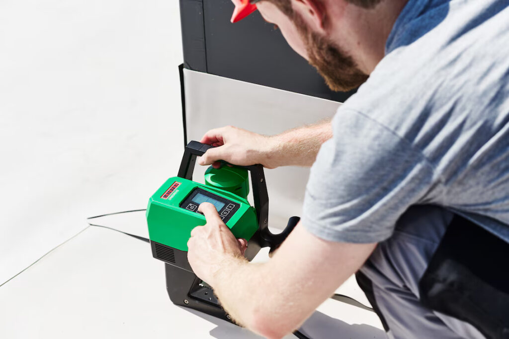 Técnico de cobertura ajustando o equipamento Leister UNIDRIVE 500 para soldagem controlada de membrana impermeabilizante em telhado plano